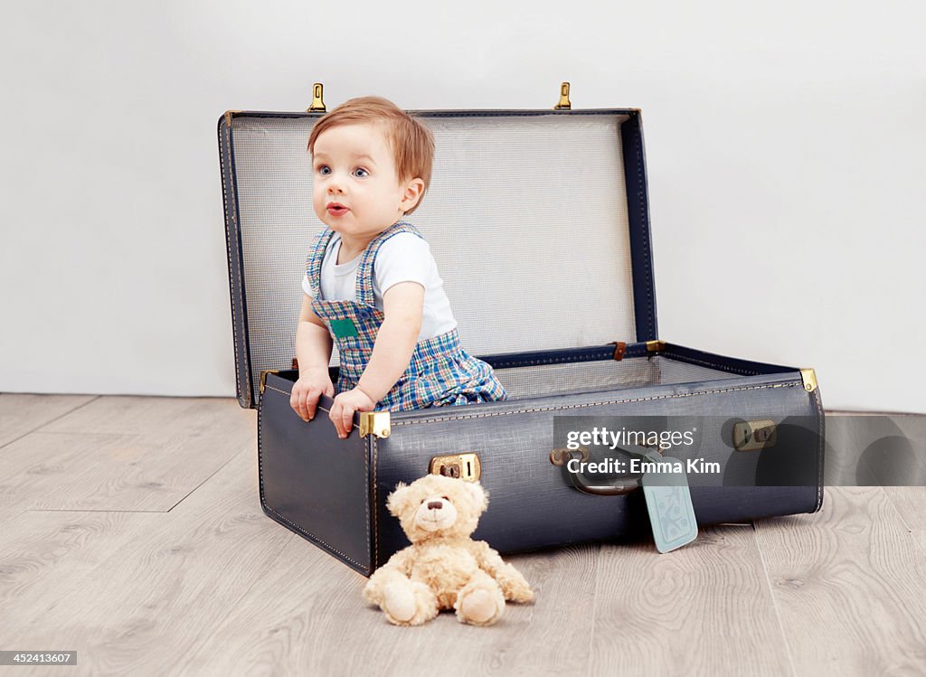 Baby boy sitting in suitcase