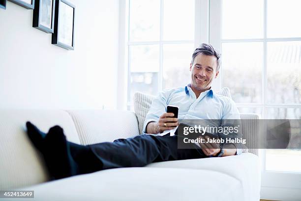 man relaxing on sofa using digital tablet and smartphone - business man smartphone tablet stock-fotos und bilder