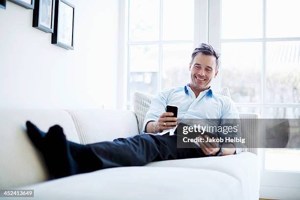 man relaxing on sofa using digital tablet and smartphone - mature man using phone tablet stock pictures, royalty-free photos & images