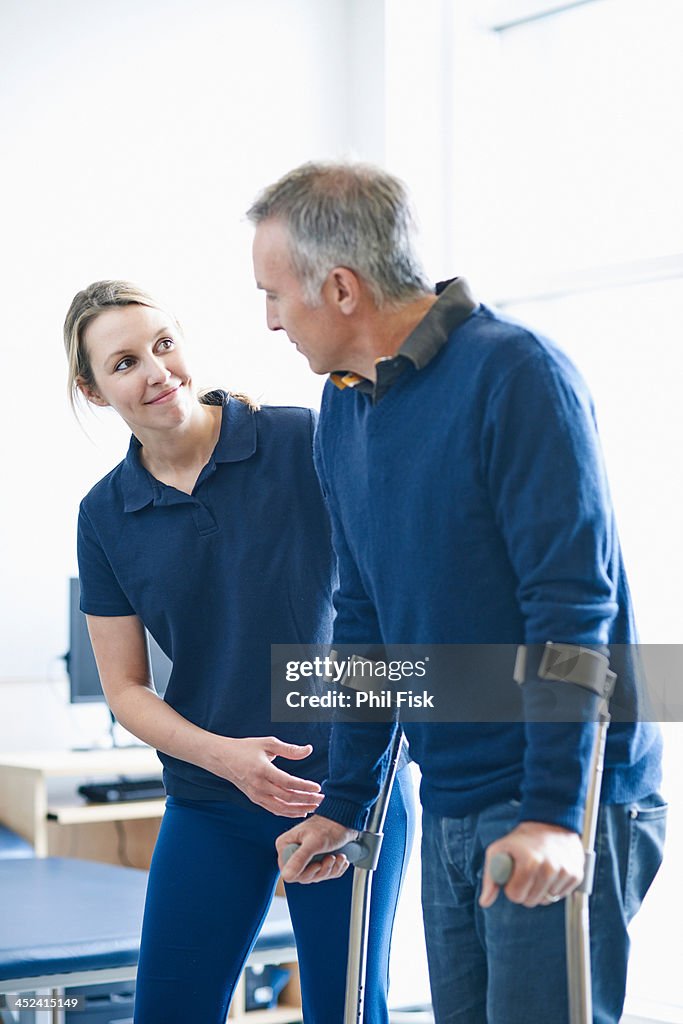Man walking using crutches, guided by therapist