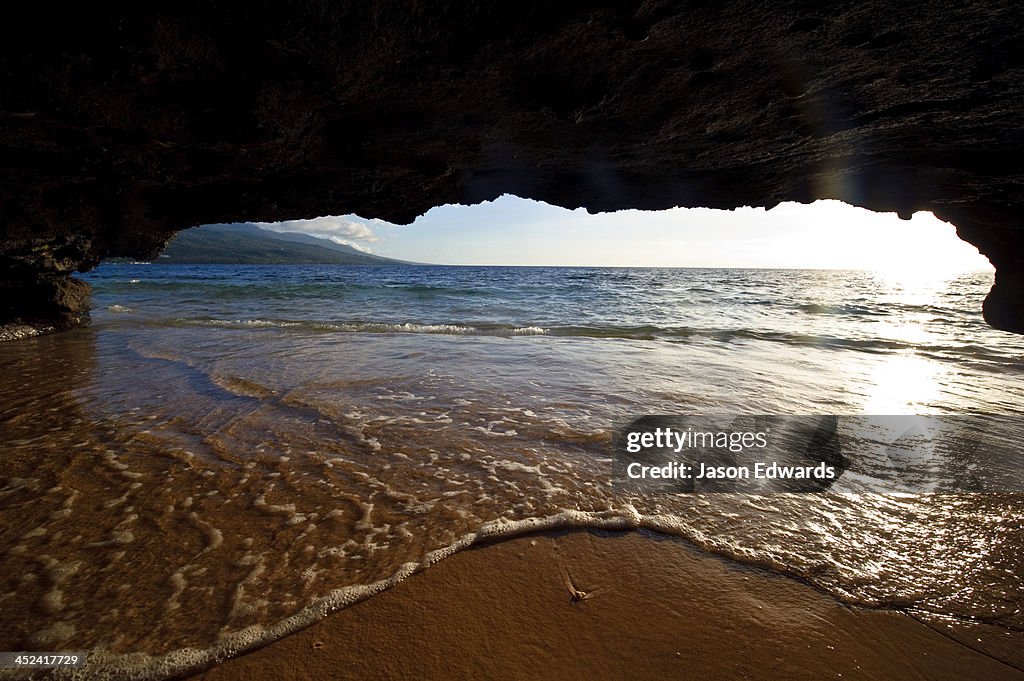 The lip of a foamy wave laps a sandy beach inside an ocean cave.