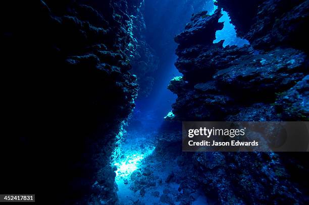 an underwater cave leads to a sunlit canyon between coral reefs. - océan-pacifique photos et images de collection