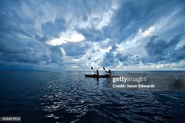 a couple paddles a sea kayak across a calm ocean beneath a storm. - canoe stock-fotos und bilder