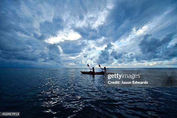 a couple paddles a sea kayak across a calm ocean beneath a storm. - canoe ストックフォトと画像