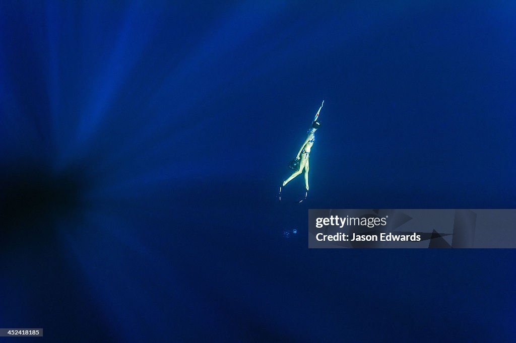 A free-diver swims through sun rays in the vast ocean depths.