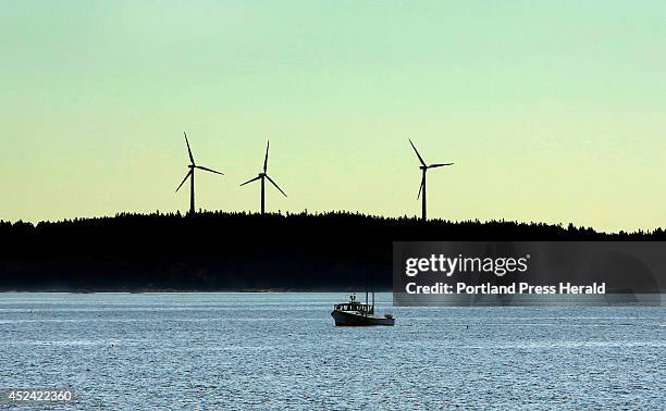 Lobster boat plies the waters off Vinalhaven where three wind turbines, which came on line five years ago, are still causing controversy. Residents...