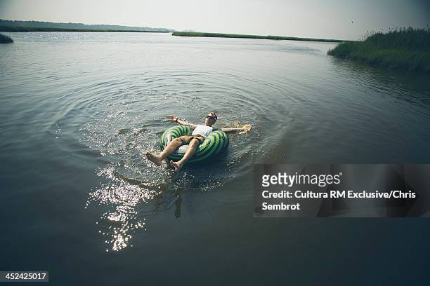 man lying in inflatable ring in river, arms outstretched - rubber ring stock pictures, royalty-free photos & images