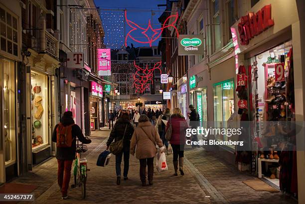 Shoppers walk underneath festive Christmas lights as logos for T-Mobile, operated by Deutsche Telekom AG, left, and Specsavers Optical Group Ltd.,...