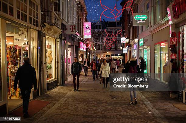 Shoppers walk underneath festive Christmas lights as logos for T-Mobile, operated by Deutsche Telekom AG, left, and Specsavers Optical Group Ltd.,...