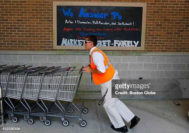 Market Basket employee Chris Conte pushes a stack of shopping carts past a sign in support of ousted Market Basket president Arthur T. Demoulas...