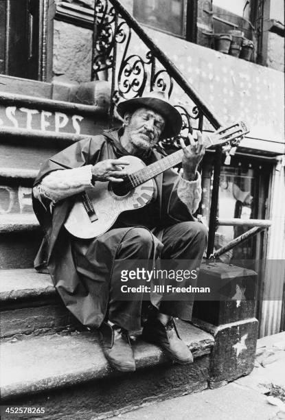 Homeless man plays a small guitar on the steps of an apartment block on MacDougal Street, Greenwich Village, New York City, 1972.