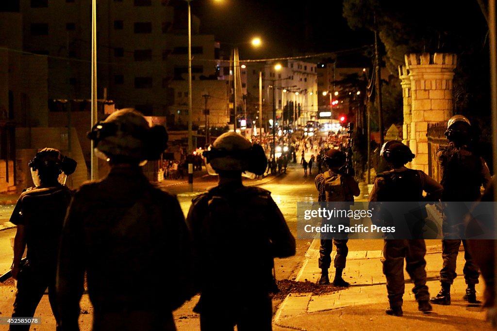 Israeli soldiers look on as Palestinian youth gather...