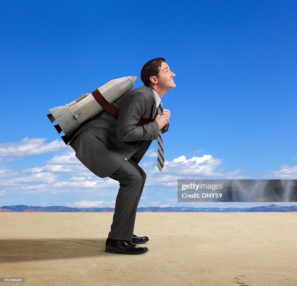 Businessman standing with rocket strapped to his back in desert