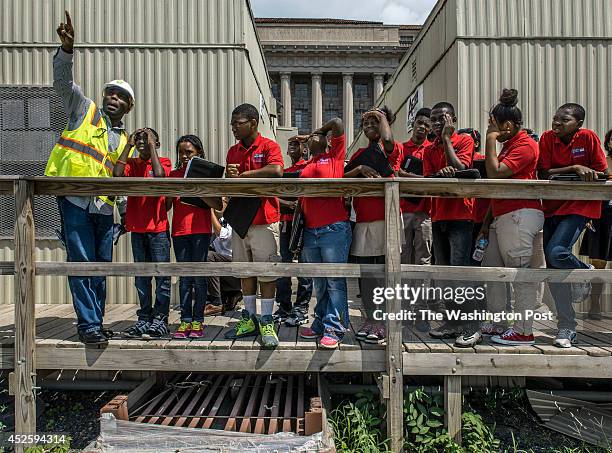 Michael Ajomale, Structural Engineer, left, shows Middle school students from Browne Education Campus, squinting in harsh sunlight, nuances of the...