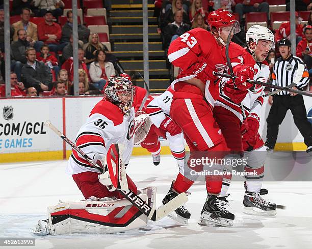 Goaltender Justin Peters of the Carolina Hurricanes looks for the puck as teammate Justin Faulk battlles in front with Darren Helm of the Detroit Red...