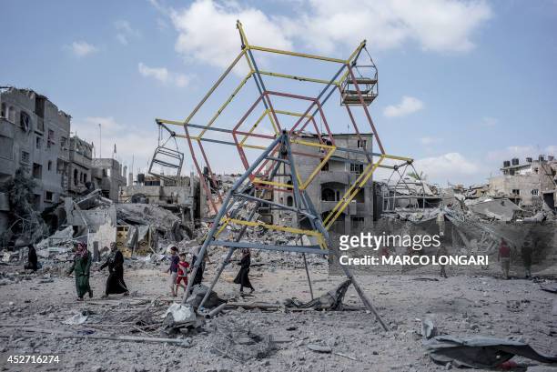 Palestininans go their way past rubbles and a mini ferris wheel in the northern district of Beit Hanun in the Gaza Strip, during an humanitarian...