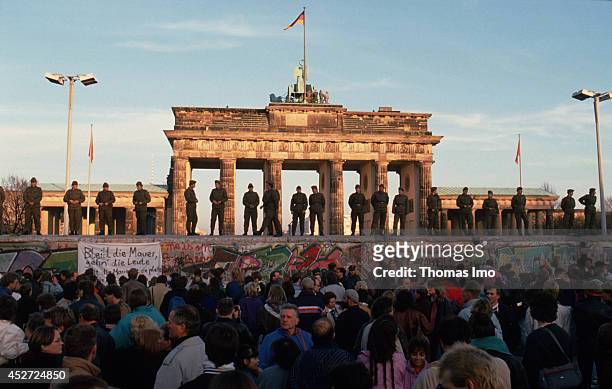 Border guards of the German Democratic Republic standing on the Berlin Wall observing demonstrating people on November 09 in Berlin, Germany. The...