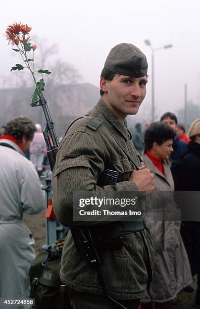 Border guard of the German Democratic Republic with a red flower in his gun barrel after opening of the border on November 09 in Berlin, Germany. The...