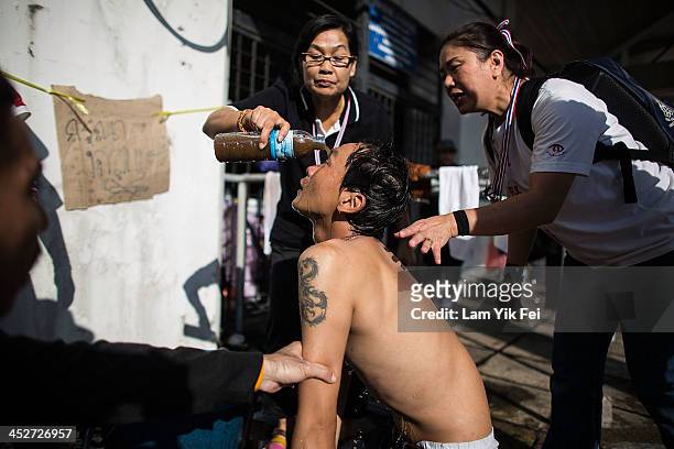 Protestors wash the eyes of anti-government protester suffering from exposure to tear gas fired by riot police on December 1, 2013 in Bangkok,...