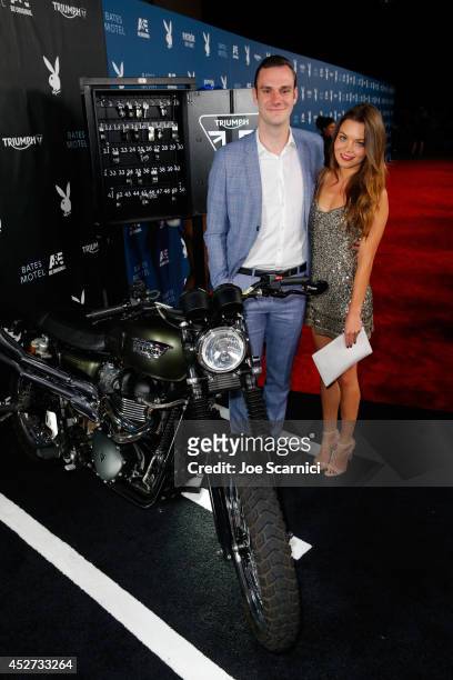 Cooper Hefner and actress Scarlett Byrne attempt to start the engine for charity of the Triumph Scrambler Custom on display at the Playboy and A&E...