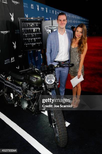 Cooper Hefner and actress Scarlett Byrne attempt to start the engine for charity of the Triumph Scrambler Custom on display at the Playboy and A&E...