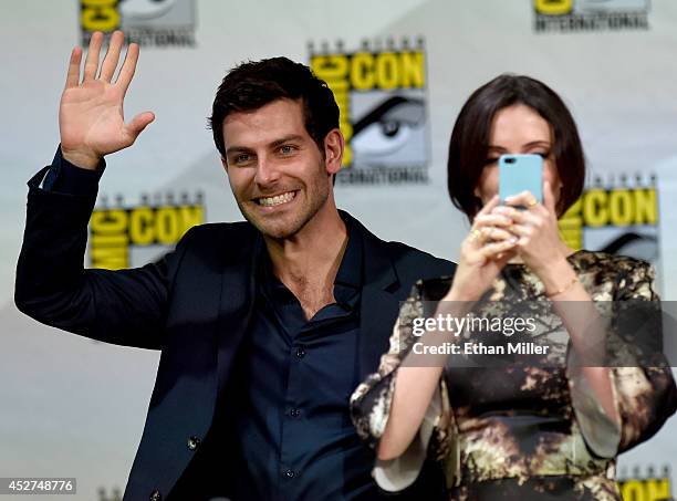 Actor David Giuntoli waves as actress Bitsie Tulloch takes images of the audience at the "Grimm" season four panel during Comic-Con International...