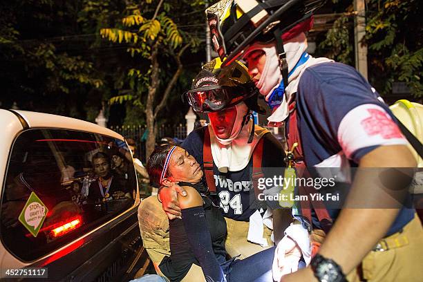 An anti-government protester is helped after being injured after riot police fire tear gas on December 1, 2013 in Bangkok, Thailand. Anti-government...