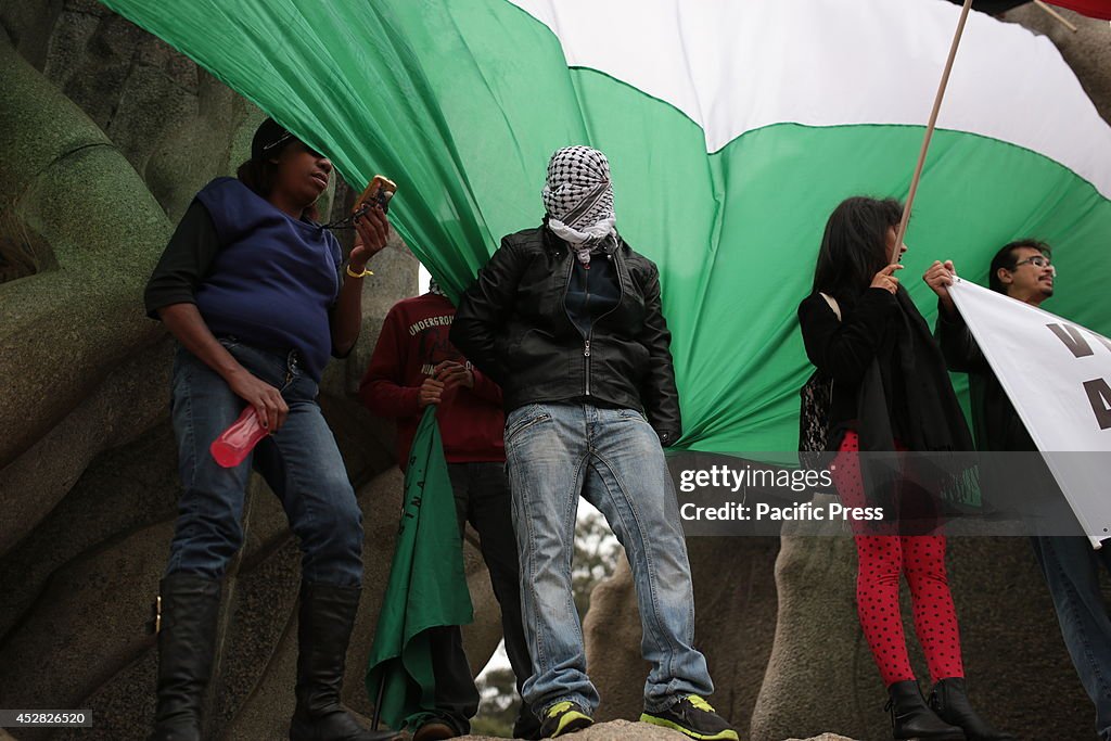 People stand on the top of a momument with Palestinian flags...