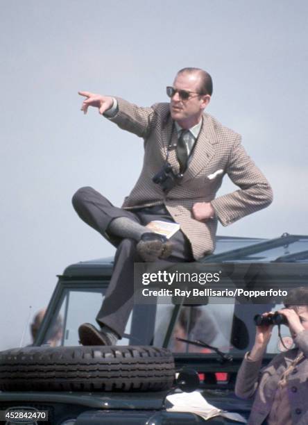 Prince Philip, the Duke of Edinburgh, pointing atop of a Land Rover whilst his wife, Queen Elizabeth II, looks through binoculars, during the...