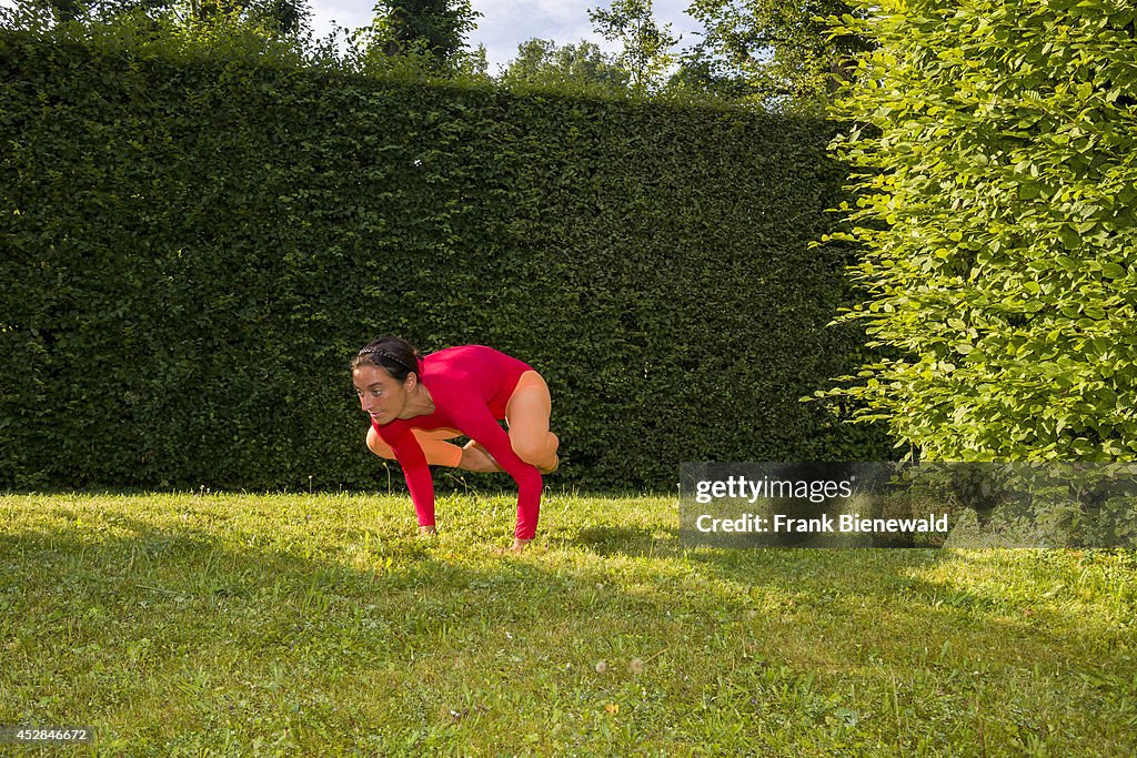 Young woman, wearing a red-orange body suit, is practising...