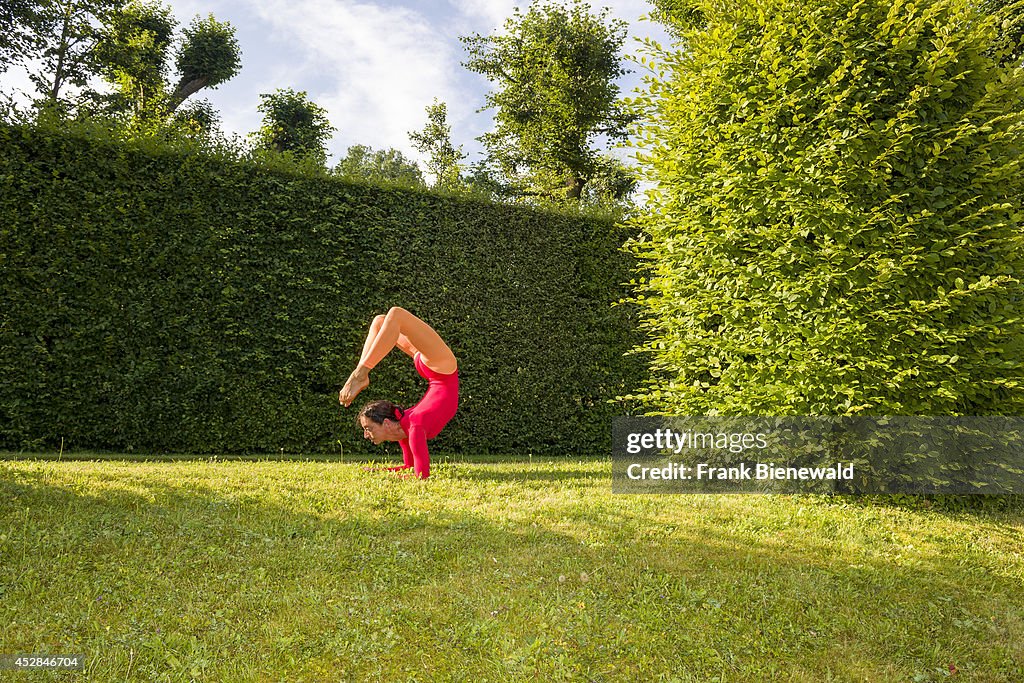 Young woman, wearing a red-orange body suit, is practising...