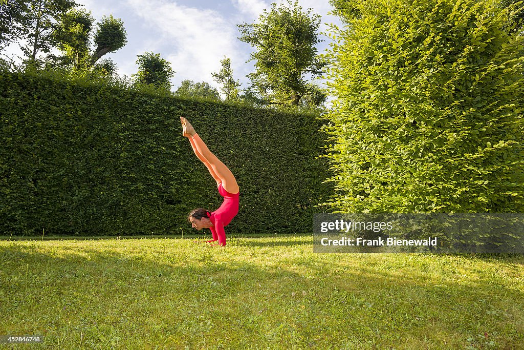 Young woman, wearing a red-orange body suit, is practising...