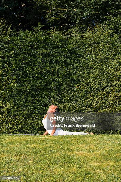 Young woman, wearing a white body suit, is practising Hatha-Yoga outdoor between trees, showing the pose: bhujangasana, cobra pose.