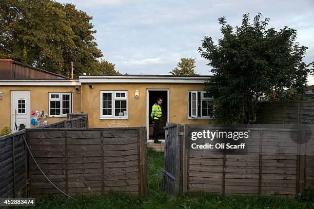 Police community support officer stands guard outside an occupied dwelling constructed in the back garden of a house as it is raided by Home Office...