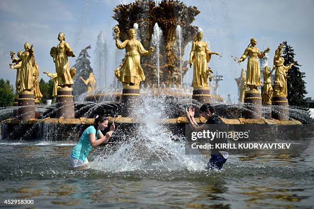 Young people splash water at each other while standing in the pool of famous "Druzhba narodov" fountain at the VDNKh, a public park and exhibition...