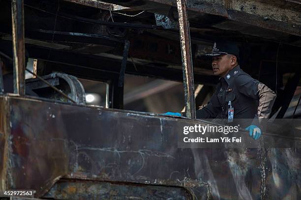 Policeman inspects a burnt bus after Anti-government protesters attack pro-government red shirt supporters at Ramkhamhaeng area on December 2, 2013...