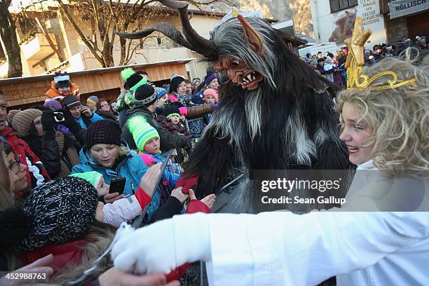 Member of the Haiminger Krampusgruppe dressed as the Krampus creature accompanies little girls dressed as angels distributing sweets to children...