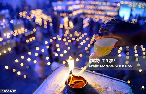 Hindu devotee pours oil into a wick lamp at a temple for the Hindu God Shiva during the "Karthigai Deepam" in Bangalore on December 2, 2013....