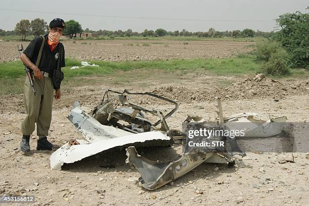 Pakistani policeman stands beside remnants of a destroyed car after an improvised explosive device exploded near the village of Maddi, outside Dera...