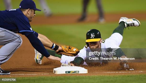 Eric Sogard of the Oakland Athletics dives into third base safe, beating the tag of Evan Longoria of the Tampa Bay Rays in the bottom of the fourth...