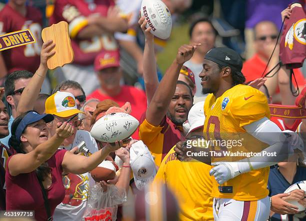Washington quarterback Robert Griffin III , right, runs toward the crowd to sign autographs during day 12 of the Washington Redskins training camp...