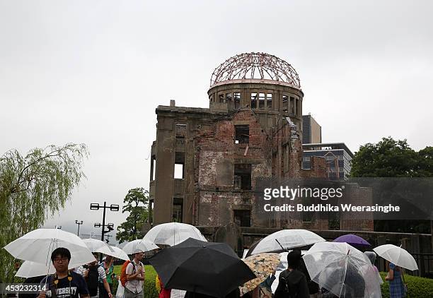 People walk in rain in front of the Hiroshima Peace Memorial, commonly called the Atomic Bomb Dome, at the Hiroshima Peace Memorial Park on the day...