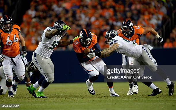 Quarterback Brock Osweiler of the Denver Broncos braces for a hit from defensive end Cassius Marsh of the Seattle Seahawks on the right and defensive...