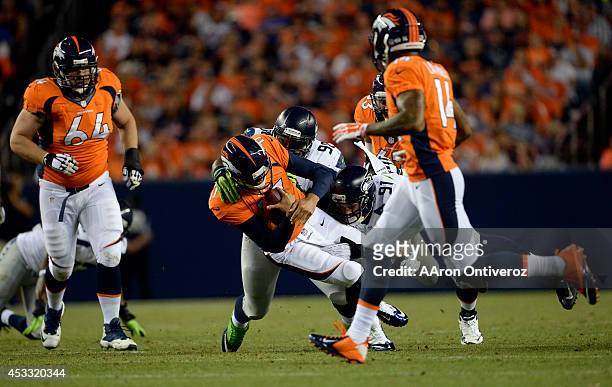 Quarterback Brock Osweiler of the Denver Broncos gets hit by defensive end Cassius Marsh of the Seattle Seahawks on the right and defensive end Greg...
