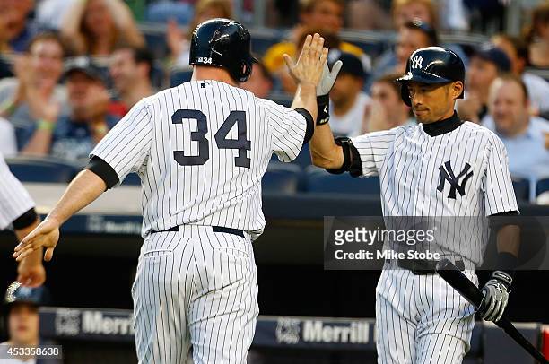 Brian McCann of the New York Yankees is greeted by Ichiro Suzuki after scoring on Martin Prado RBI single in the first inning against the Cleveland...