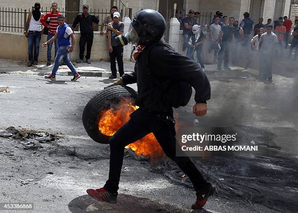 Palestinian demonstrator carries a burning tire during clashes with Israeli soldiers at the entrance of the Jewish settlement of Psagot near the...