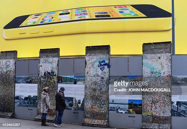 People check out a segment of the Berlin wall at Potsdamer Platz as a giant billboard advertises an iPhone 5C, in Berlin December 4, 2013. AFP PHOTO...