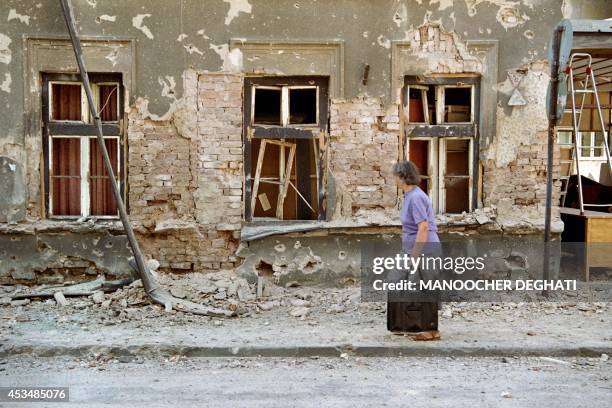 Sarajevo resident walks past a damaged house in fornt of the french hospital in Sarajevo, on August 26, 1992. A nurse was killed in the hospital when...