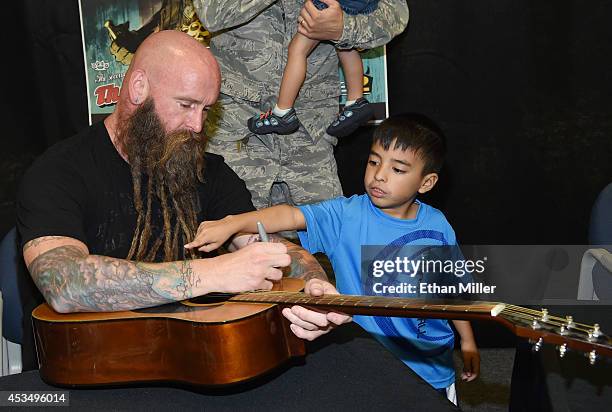 David Gregorich points at bassist Chris Kael of Five Finger Death Punch while he signs a guitar at Nellis Air Force Base as the band highlights its...