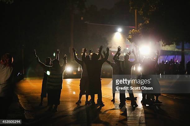 With their hands raised, residents gather at a police line as the neighborhood is locked down following skirmishes on August 11, 2014 in Ferguson,...